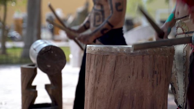 Extreme closeup of Mayan or Aztec drummers playing wooden drums with animals skins and sticks in a park in Valladolid, Mexico.