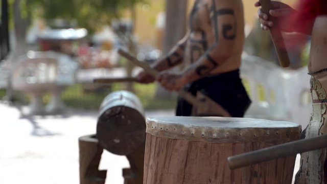 Extreme closeup of Mayan or Aztec drummers playing wooden drums with animals skins and sticks in a park in Valladolid, Mexico.