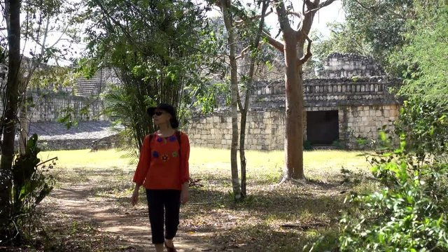 Camera in front of a woman looking at the ruins of Ek Balam archaeological park on a windy and sunny day.