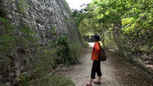 Camera following a woman walking on the jungle trails around the Acropolis at Ek Balam archaeological park in Yucatan, Mexico.