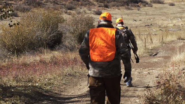 Father and Son Hunters walk down path with rifle and backpack. Two Shot. Slow Motion. 4K