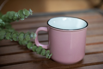 A mug on a wooden table and a branch of eucalyptus