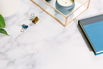 Home office desk flat lay with books, clips, candle, and potted house plant on marble surface with copy space / Freelance work concept