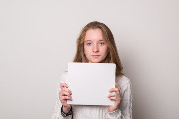 Positive girl holds a blank poster for text. Schoolgirl with a smile holds a white sheet for text.