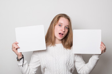 Positive girl holds a blank poster for text. Schoolgirl with a smile holds a white sheet for text.