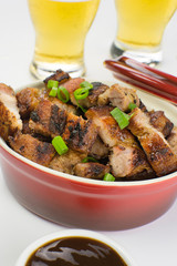 Grilled pork belly in a red bowl with barbecue salce and beer in white background close