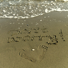 Words Don't Worry and footprints on beach sand