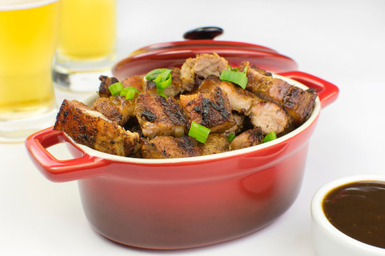 Grilled pork belly in a red bowl with barbecue salce and beer in white background