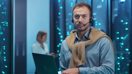 IT service support technician with laptop visually inspecting operational rack server room. His female colleague checking hardware of supercomputer in data center.
