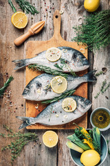 Raw dorado fish with ingredients, lemon, herbs, oil, vegetables and spices on wooden cutting board over wood background. Top view. Healthy food diet. Food pattern. Seafood concept.