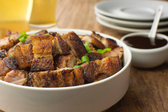 Grilled pork belly in a white bowl with barbecue salce and beer in wood pub table background close