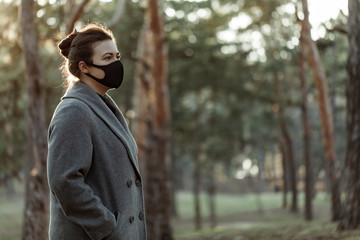 Woman in medical mask posing on the camera on the trees background. Girl uses a protective mask against a viral infection. Outdoor