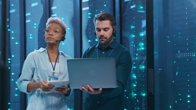 Professional Diverse Team Of Data Center Specialists Coworking In Server Room. Female And Male Engineers Inspecting Internet Database Servers At Computer Security. Teamwork.