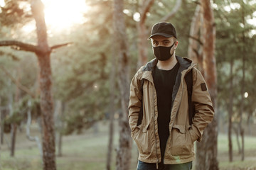 man in black medical mask and in cap posing on the camera on trees background. Man looking at camera. Health care. Epidemy