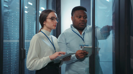 Multi-ethnic male and female administrators opening rack server cabinet inspecting supercomputer...
