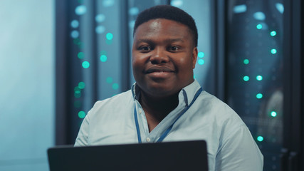 African american system administrator using laptop working in digital server rack corridor of computer security rom. Data center specialist. Information technology.