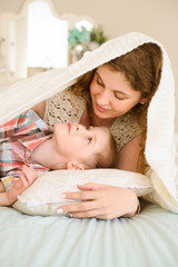 Mom gently looks at her son. they lying on bed covered with bedspread in bright bedroom. She hugs child carefully