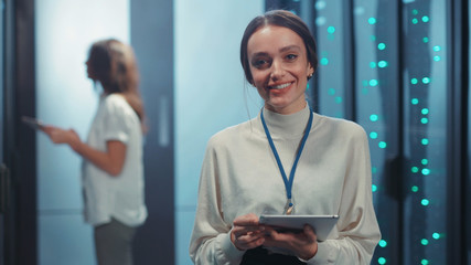 Joyful pretty young woman IT technician holding tablet staying at modular data center. Portrait of...