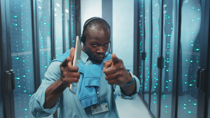 Ecstatic black IT specialist having fun in data center dancing with joy in high tech server room corridor. People and technology. Fun concept.