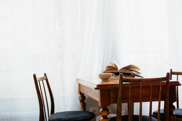 wooden table and chairs with a Cup and books on the table in front of the window with daylight