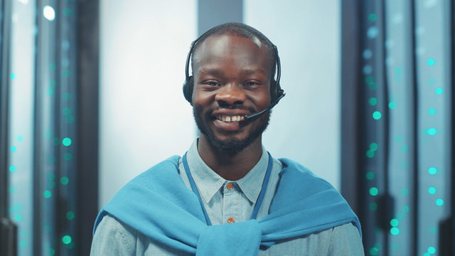 Cheerful african american server engineer standing in digital corridor of server room. Indoor portrait ambitious black specialist working at network and data center.