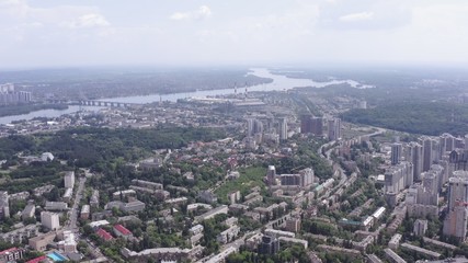 Fototapeta premium smooth drone take-off up over the summer streets of the green city (Kiev) against the background of the big river (Dnipro) Ukraine