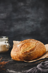 Traditional rustic sourdough bread on a craft paper and jar of flour. Baked artisan bread on black...