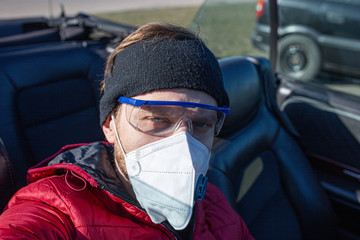male driver in a convertible in a protective medical mask and glasses, a coronavirus pandemic.