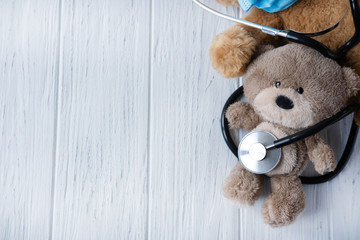 Background for banner of pediatric clinic. Treatment of childhood diseases. Toy bear with a stethoscope on a light wooden background. View from above. Children health.