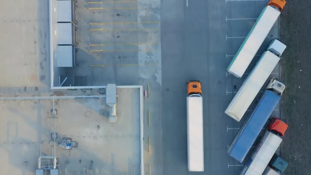 Aerial top down view of a semi-trailer truck travelling along a modern warehouse