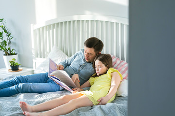 Father reading book to daughter on bed in bedroom. Concept of quarantine, pandemic, coronavirus, lifestyle, digital detox. Stay at home