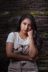 young black-haired latina leaning against a tree with a dark background