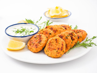 Fish cakes on a plate with lemon wedges, salad and sauce. Side view white background. 