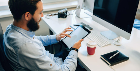 Upper view portrait of a bearded caucasian man using a tablet with blank space while drinking a coffee in his office