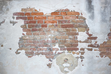 A wall of brick on which stucco partially peeled off