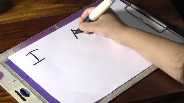 A girl is writing text I am sorry on the paper with big pen.