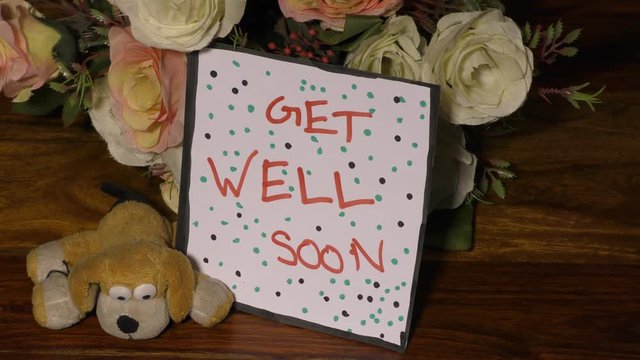 Get well soon card with dots and flowers with soft toy dog on the floor.