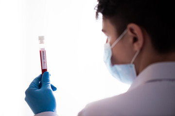 Test tube in male hand close up, doctor in medical mask holding vial with red liquid. Concept blood...