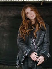 Happy young redhead woman posing outdoors on dark blurred background enjoying fresh cold spring day on city stroll