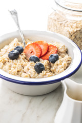 Bowl of oatmeal porridge with strawberries and blueberries.