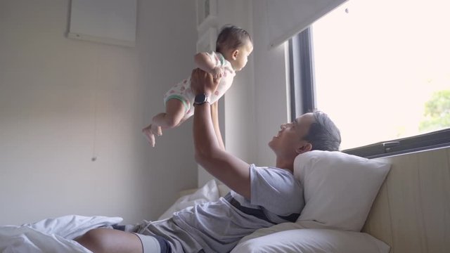 asian father picks up his daughter's baby when enjoying playing on the bed