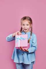 Joyful little girl holding pink present in hands on pink backgorund