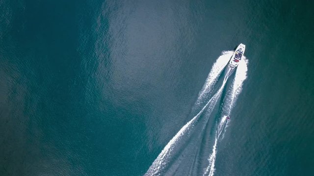 Aerial drone tracking shot of a speed boat and a man waterskiing doing water sports in Velden Am Worthersee lake, Austria on a beautiful sunny day mountain view 