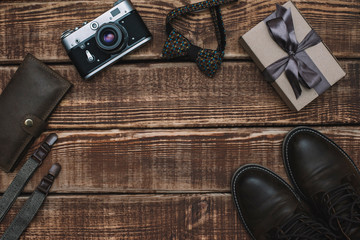 Fototapeta na wymiar Gift box for father's day with men's accessories bow tie, wallet, retro camera, suspenders and leather shoes on a wooden background. Copy space. Flat lay.
