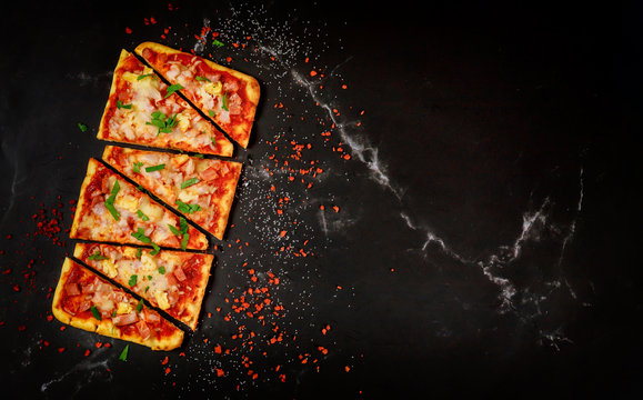 Sliced Hawaiian pizza on black stone background, top view.
