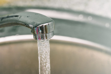 Open the tap water from the tap. Water flows from a chrome tap to the sink. Copy space.