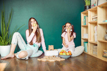 Two sisters in medical mask eating apple at home during covid quarantine. Stay at home Coronavirus epidemic concept.