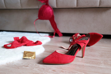 Red shoes on high heels, lace panties, bra and condom on the fur rug on a floor near sofa. Concept...
