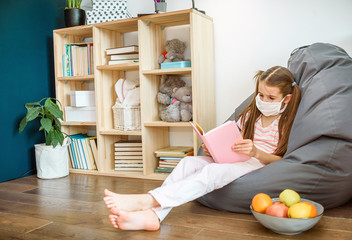a girl in medical mask siting on wood floor and reading a books during quarantine