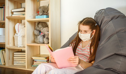 a girl in medical mask siting on wood floor and reading a books during quarantine